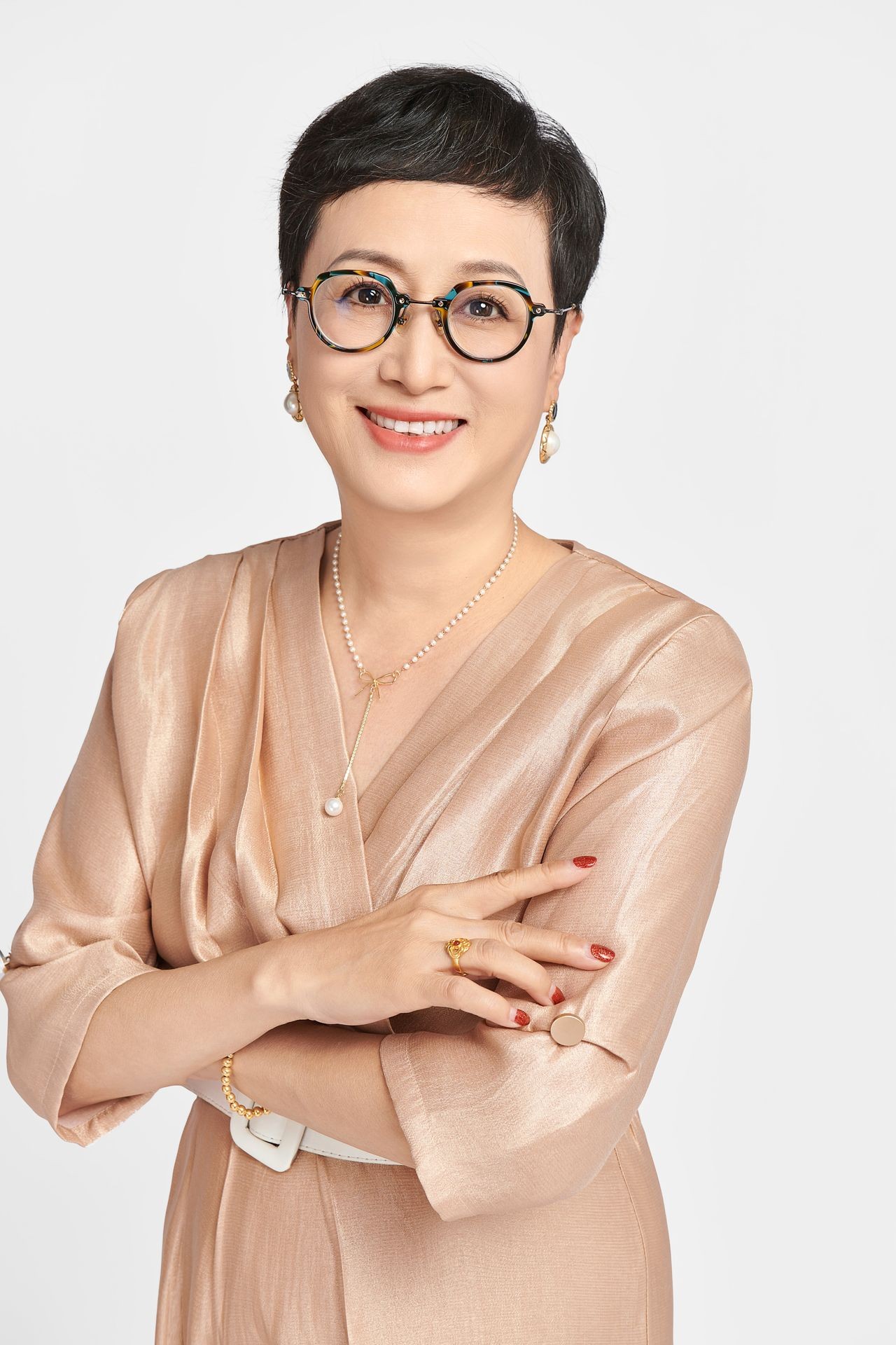 Smiling person with short hair, wearing glasses and gold earrings, in a shiny beige outfit.